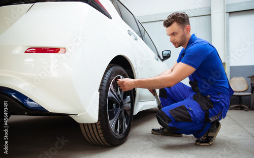 Car mechanic with a tablet in his hand and working overalls checks the condition of tires after changing