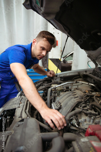 Cheerful, handsome, and confident car repair specialist in overalls repairs and replaces old parts with new ones in a car on a lift in service