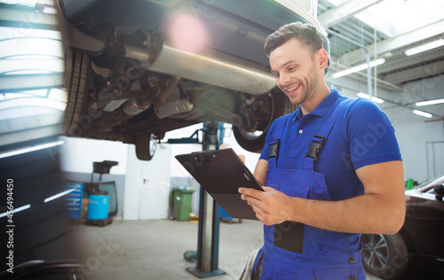 Confident and concentrated young and experienced car repair specialist with a tablet in his hand inspects and diagnosis the car for breakdowns