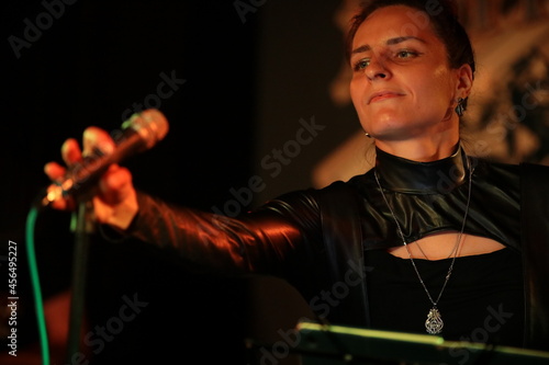 Portrait of a person with a microphone singer a young beautiful brunette woman in black working on stage in a nightclub.Image of a pretty girl professional artist rock musician close up