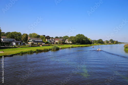 View over river Alblas on meadow with residential houses against blue cloudless summer sky - Alblasserdam, Netherlands photo