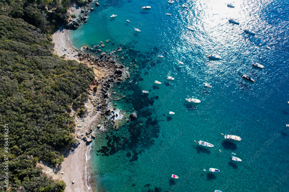View from above, stunning aerial view of a bay with boats and luxury yachts sailing on a turquoise, clear water surrounded by cliffs. Porto Santo Stefano, Monte Argentario, Italy.