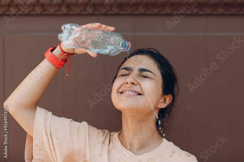 Stressed woman suffering of heatstroke and refreshing pouring with cold water outside. Weather abnormal heat concept photo