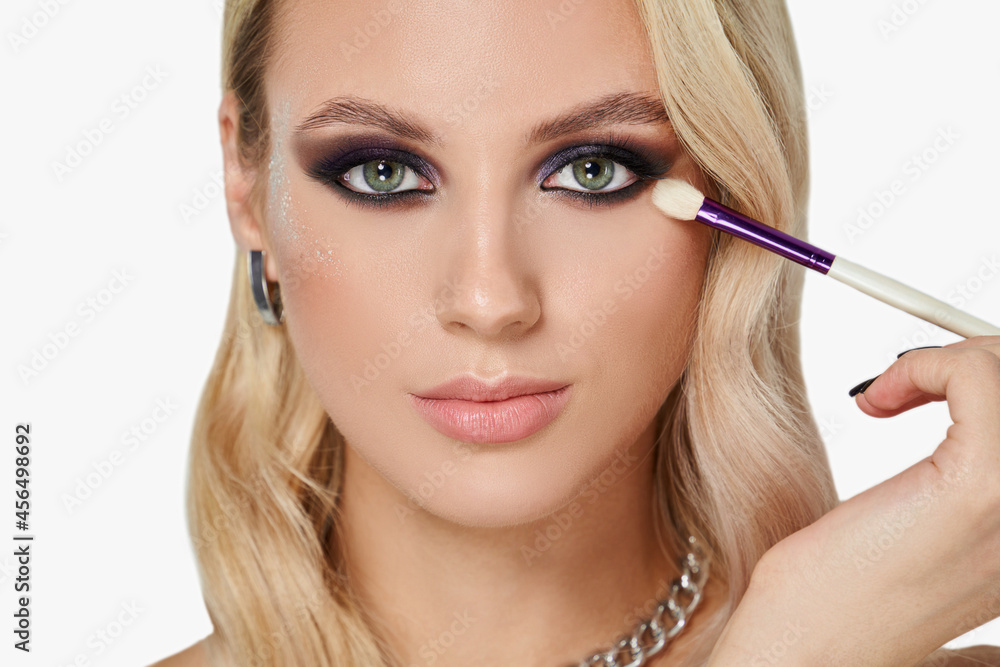 Portrait of blonde woman with smokey eyes make-up and wavy hairstyle. Appilying brush.