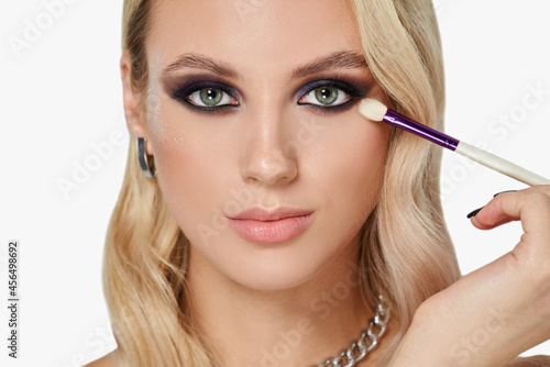 Portrait of blonde woman with smokey eyes make-up and wavy hairstyle. Appilying brush.