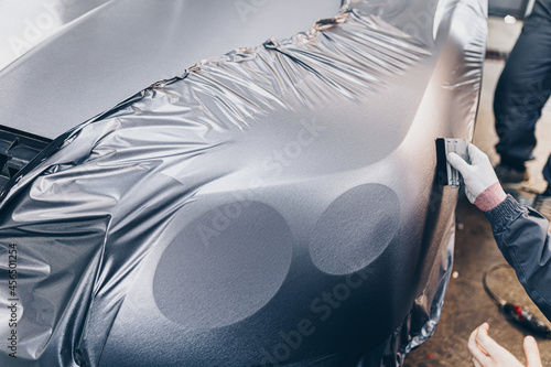 Car wrapping specialist putting vinyl foil or film on car. Selective focus. .