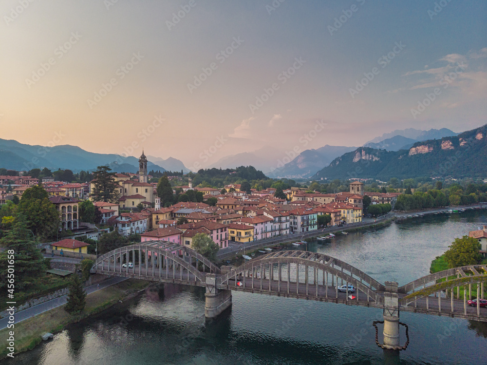 Aerial view of cute little Italy village on the banks of the blue river with a bridge in the foreground, Italy