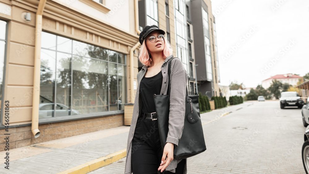 Stylish young beautiful woman with glasses and a hat in fashion clothes with a shirt and black jeans with a bag walks in the city Stylish young beautiful woman with glasses and a hat in fashion clothes with a shirt and black jeans with a bag walks in the city