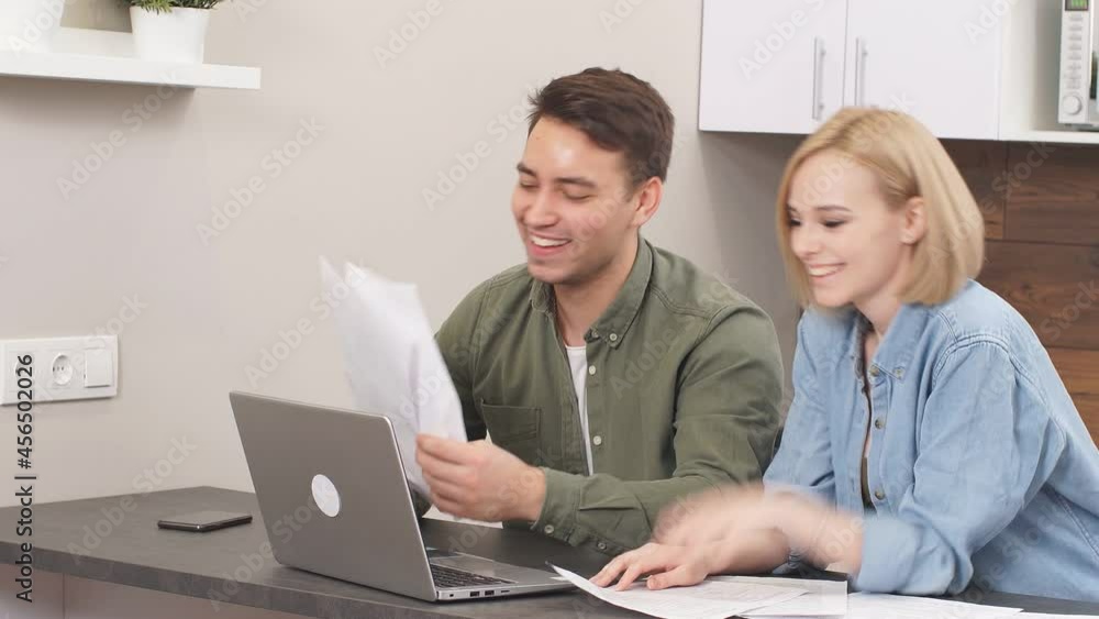 Positive funny married couple checking finance at home using laptop, sit on table with papersvv Positive funny married couple checking finance at home using laptop, sit on table with papersvv