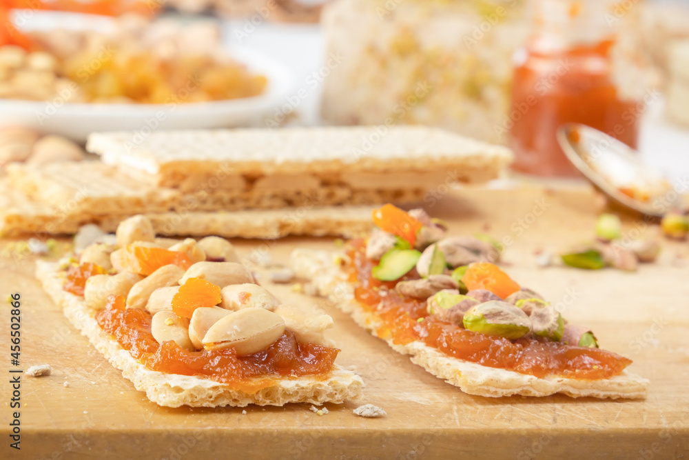 Crispy low-calorie wheat crackers with peanuts, pistachios, raisins and candied fruits on a thin layer of apricot jam on a wooden board against a background of oriental sweets. Close-up Crispy low-calorie wheat crackers with peanuts, pistachios, raisins and candied fruits on a thin layer of apricot jam on a wooden board against a background of oriental sweets. Close-up