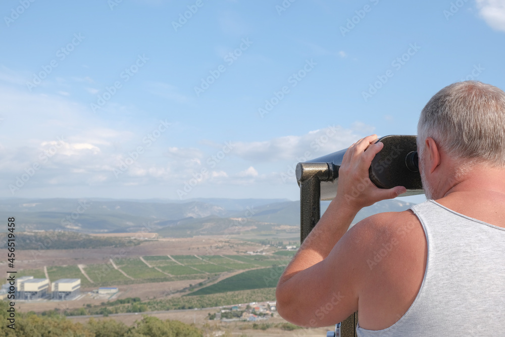 A man looks at the mountains through binoculars on the observation deck.