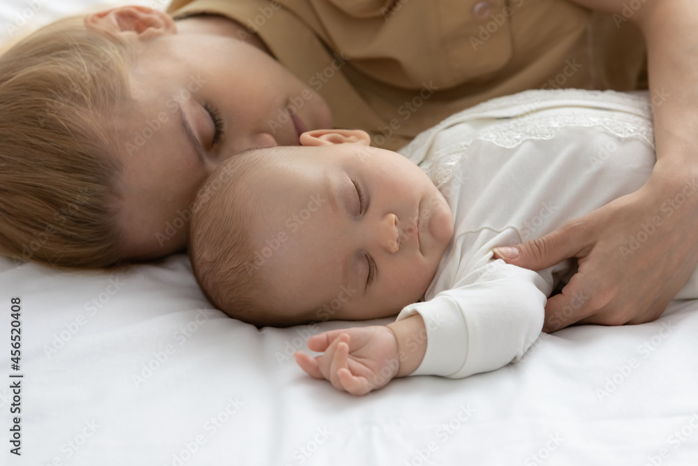 Peaceful tired mother and calm infant sleeping together, lying in bed on white linen, sheet, relaxing in bedroom, taking break. Pretty new mom relaxing near sleepy baby at home. Child care, motherhood Peaceful tired mother and calm infant sleeping together, lying in bed on white linen, sheet, relaxing in bedroom, taking break. Pretty new mom relaxing near sleepy baby at home. Child care, motherhood