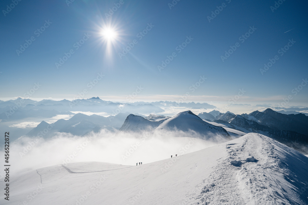 Group alpinists on an adventure ascent on high alpine peak or summit. Fog and mist weather, sharp snow ridge Climbing in high mountain landscape. Grossvenediger, Austria.