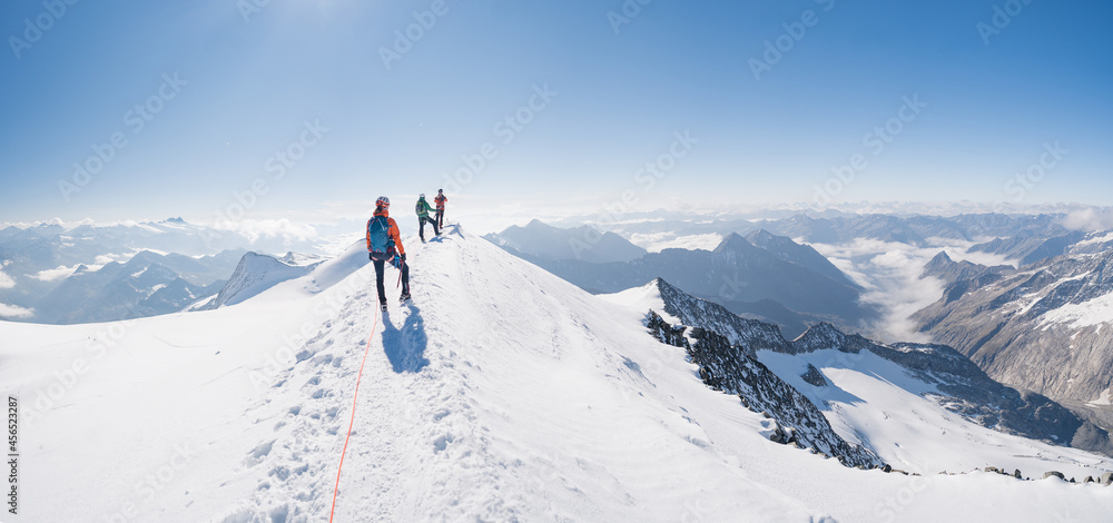 Climbers team on a trail through a dangerous glacier and avalanches in Austiran Alps. Epic moment near the top of Großvenediger glacier as the clouds disappear for a moment. - obrazy, fototapety, plakaty 