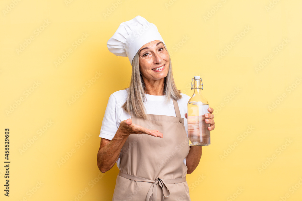 middle age chef woman smiling cheerfully, feeling happy and showing a concept in copy space with palm of hand with a water bottle middle age chef woman smiling cheerfully, feeling happy and showing a concept in copy space with palm of hand with a water bottle
