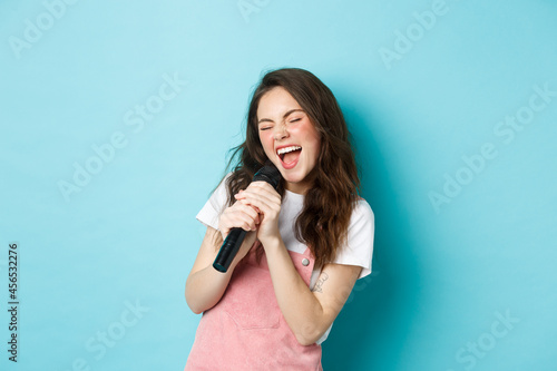 Beautiful girl singer holding microphone, singing karaoke in mic, standing over blue background