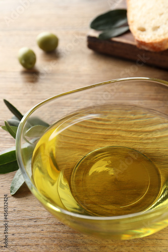 Glass bowl of olive oil on wooden table, closeup