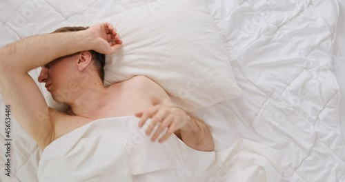 Young man tosses and turnes during sleep. Guy rolls over in bed. Restless sleep. Top view.