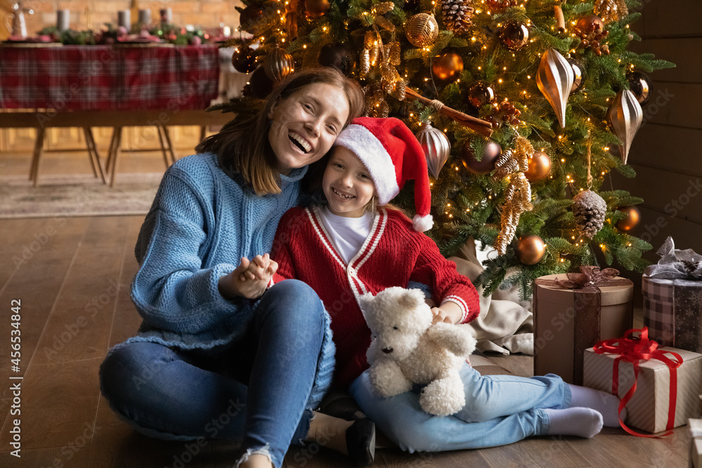 Full length image of happy two female generations bonding family in warm winter clothes sitting near decorated tree with wrapped presents, enjoying Christmas New Year winter holidays time together. Full length image of happy two female generations bonding family in warm winter clothes sitting near decorated tree with wrapped presents, enjoying Christmas New Year winter holidays time together.