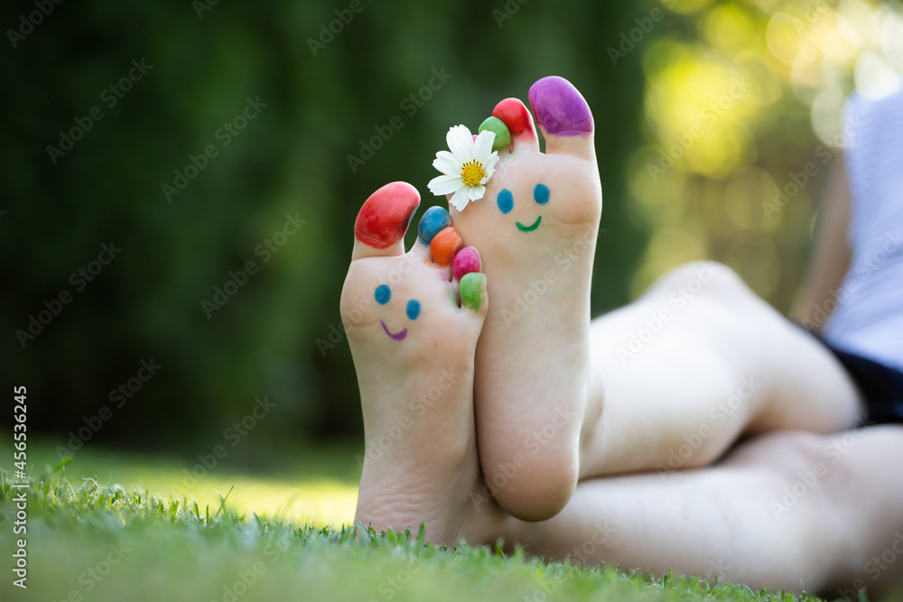 Naklejka premium Children's feet with a pattern of paints smile on the green grass.