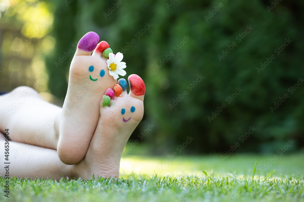 Fototapeta premium Children's feet with a pattern of paints smile on the green grass.