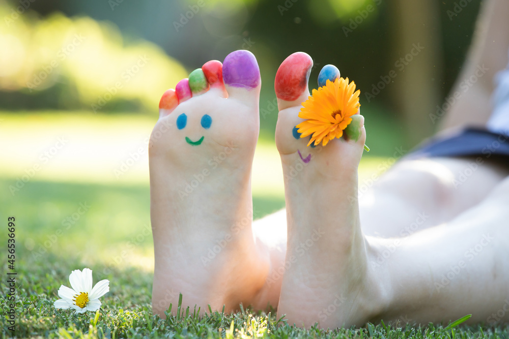 Fototapeta premium Children's feet with a pattern of paints smile on the green grass.