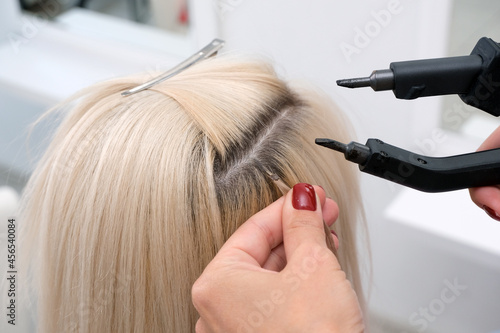 Photography hairdresser makes hair extensions to a young blonde girl in a beauty salon