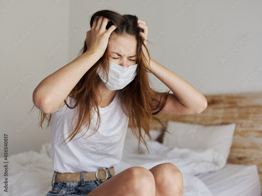 coronavirus woman in quarantine sits indoors on the bed and touches her head with her hands coronavirus woman in quarantine sits indoors on the bed and touches her head with her hands