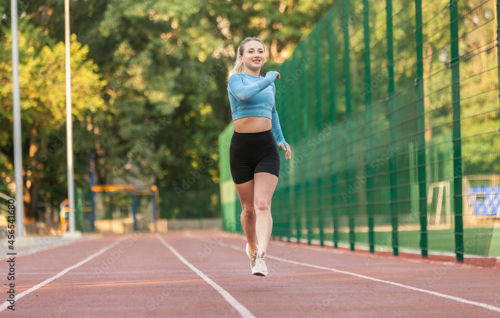 Young cheerful woman athlete runs across the stadium. Healthy lifestyle