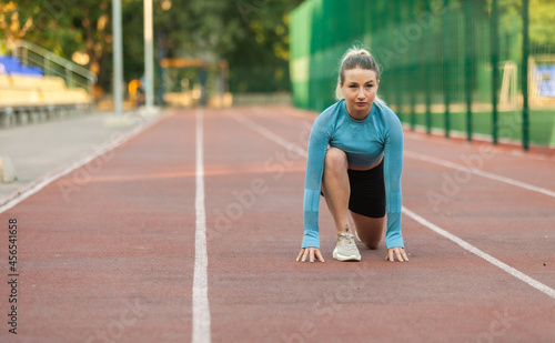 Young athletic woman runner in ready to start position at stadium