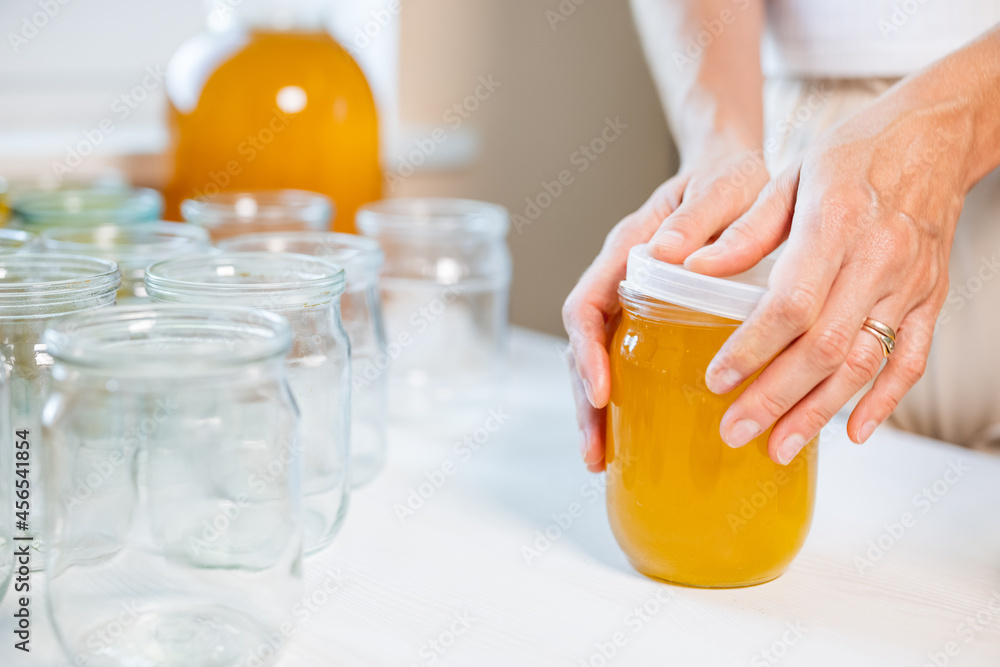 Woman's hands close the lid of a jar of honey standing on a white table and next to a saucer with a spoon Woman's hands close the lid of a jar of honey standing on a white table and next to a saucer with a spoon