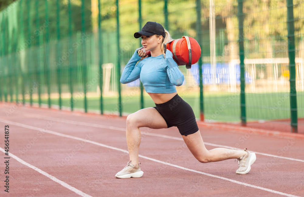 Young athletic woman workout with a heavy sand bag at the stadium in the morning