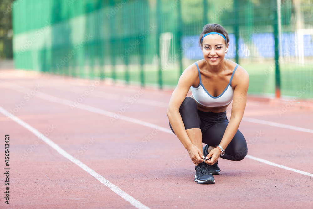 Muscular woman runner tying the laces of sneakers at the stadium