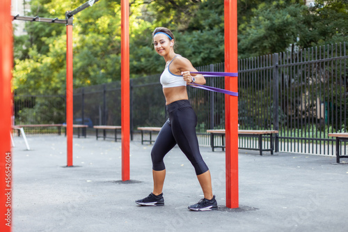 Young muscular woman trains muscles with fitness rubber bands on a sports workout ground. Healthy lifestyle. Fitness and bodybuilding. Resistance training