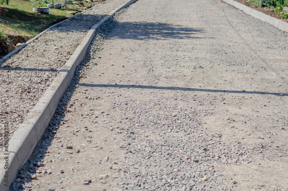 Fototapeta premium Construction of a new road and sidewalk. The roadway and walkway are filled with compacted crushed stone. Ready to be covered with asphalt or concrete. Repair and construction work.