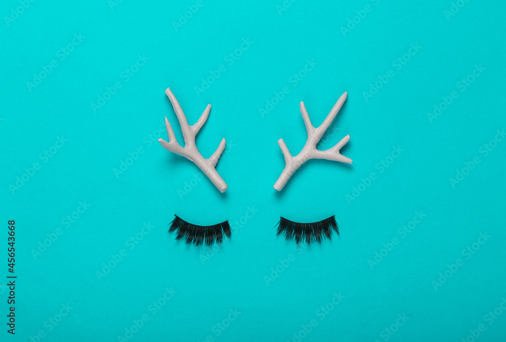 Minimal layout. Deer antlers and false eyelashes on a turquoise background. Top view. Concept art Minimal layout. Deer antlers and false eyelashes on a turquoise background. Top view. Concept art