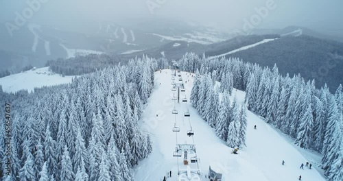 Aerial winter ski lift in mountain forest, skier going down. Flight over pine trees in white snow, slow motion. Relax for downhill skiing. Snow slopes at ski resort. Outdoor tourism. Cinematic shot