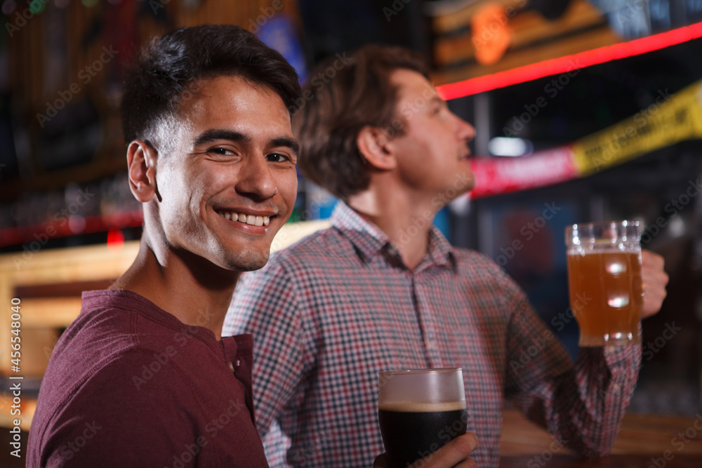 Handsome young man smiling to the camera while drinking beer with a friend