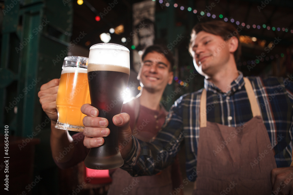 Selective focus on beer glasses in hands of professional brewers, celebrating success