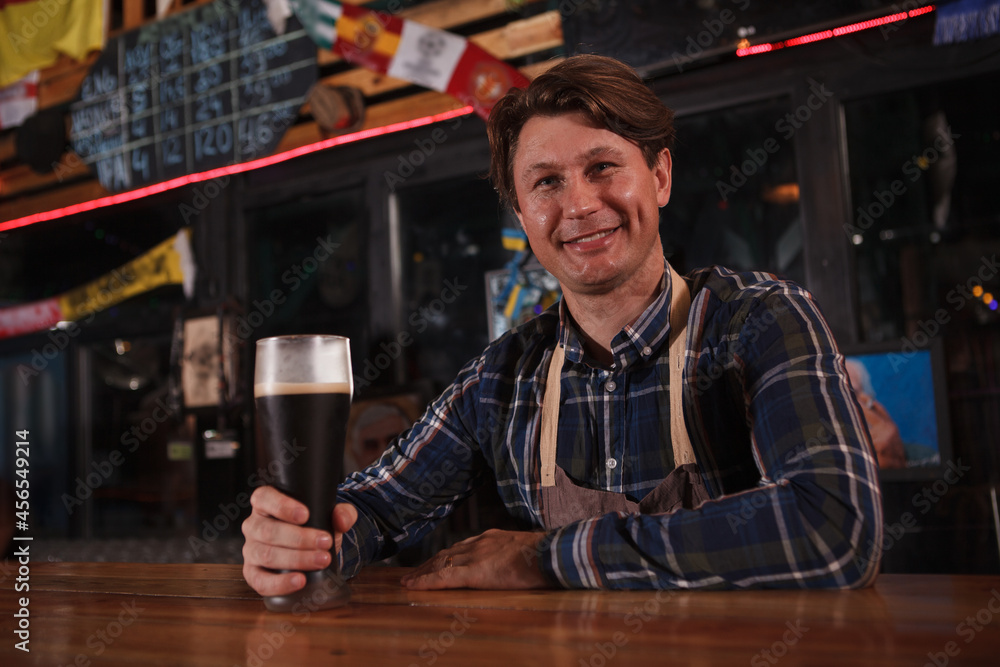Happy mature male bartender smiling to the camera, working at his beer pub