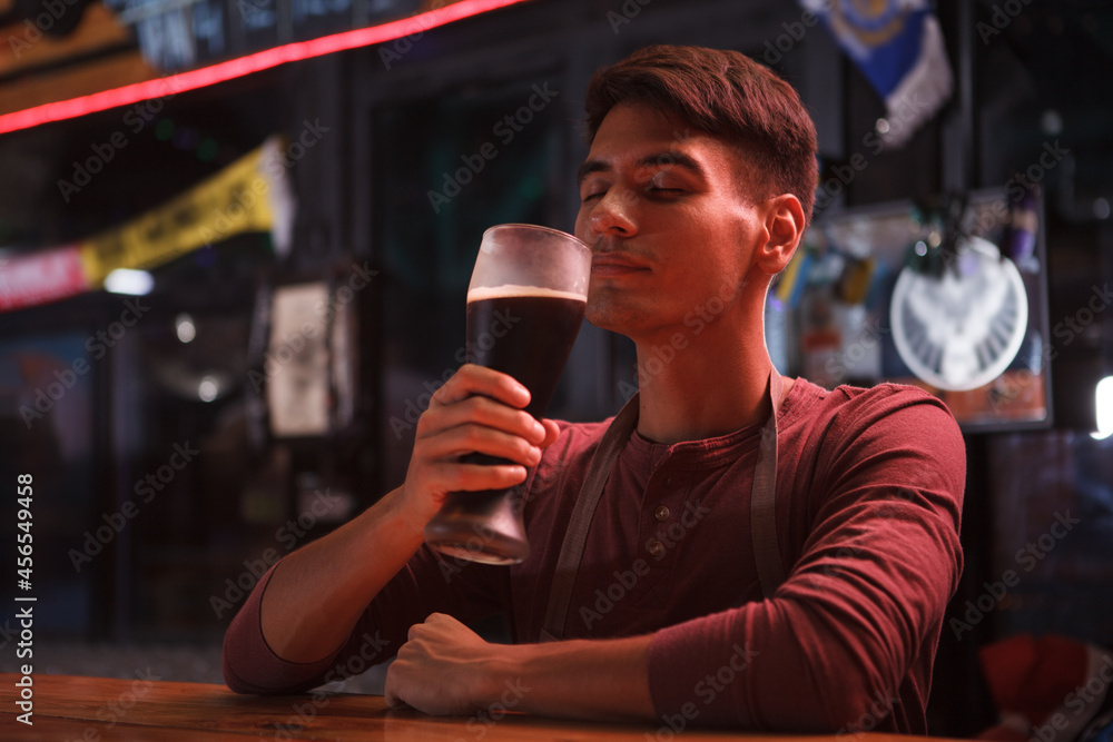 Handsome young bartender smelling aromatic craft beer while working at the pub
