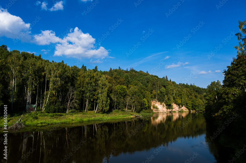 Scenic landscape of steep sandy cliff shore and green trees on it. River Gauja. National park near Sigulda in Latvia. Scenic landscape of steep sandy cliff shore and green trees on it. River Gauja. National park near Sigulda in Latvia.