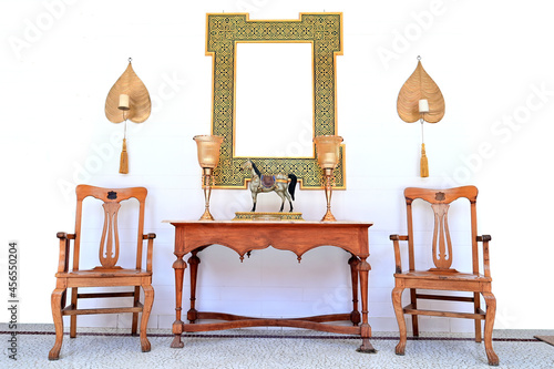 Stylish and bright retro interior with design chair   two golden lamp on table. Golden frame on the white background wall. Minimalistic concept of sitting room. Real photo.