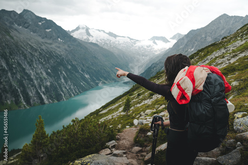 Backpacking and trekking tourism concept. Side view of female hiker tourist pointing hand on right direction. Young woman with backpack and trekking poles looking for directions in Zillertal, Austria