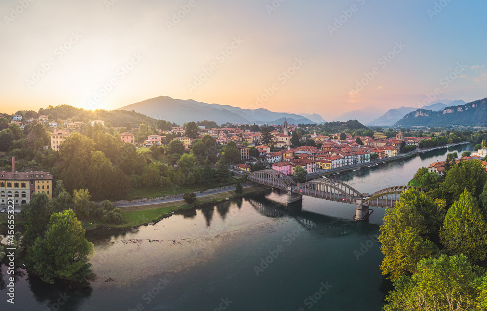 Aerial view of cute little Italy village on the banks of the blue river with a bridge in the foreground, Italy