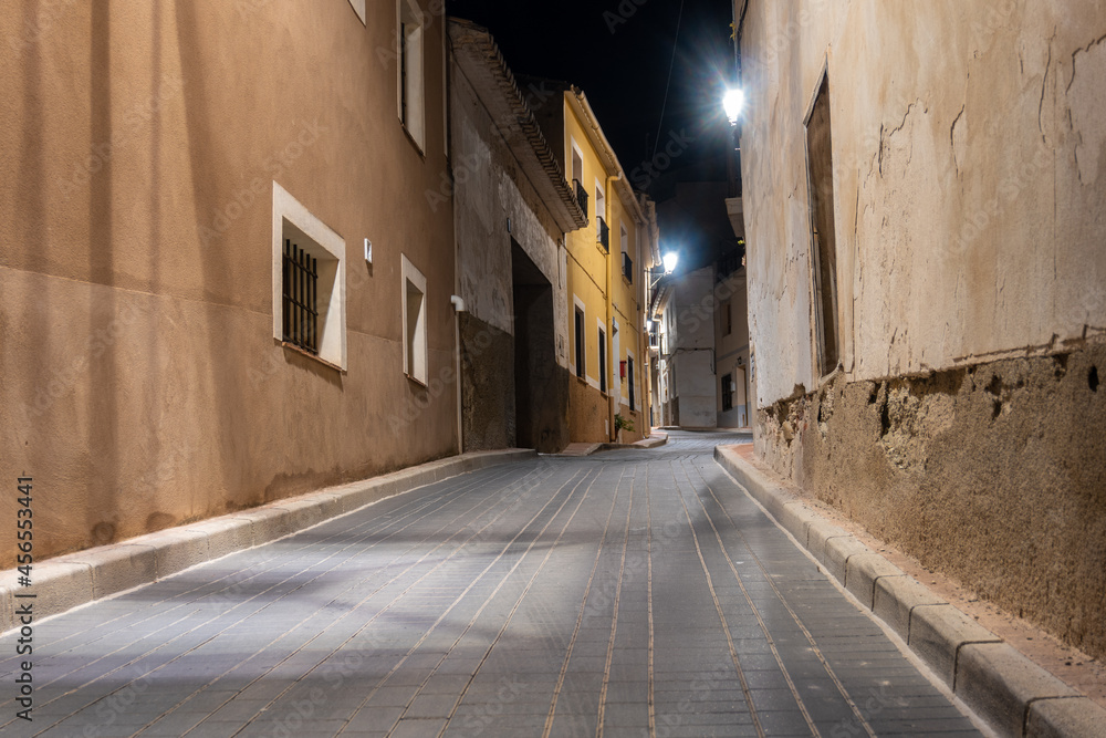 Narrow town street, empty and lit by streetlights at night.