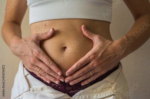 Close-up of a pregnant woman holding her hands over her nude belly. 10 weeks