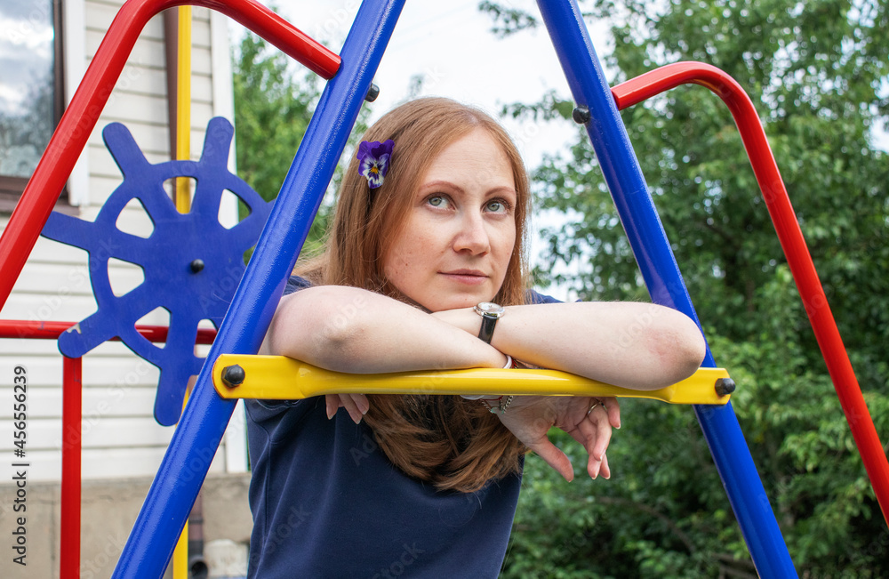 Obraz premium portrait of a young girl with red hair and a flower in her hair, sitting on a children's playground