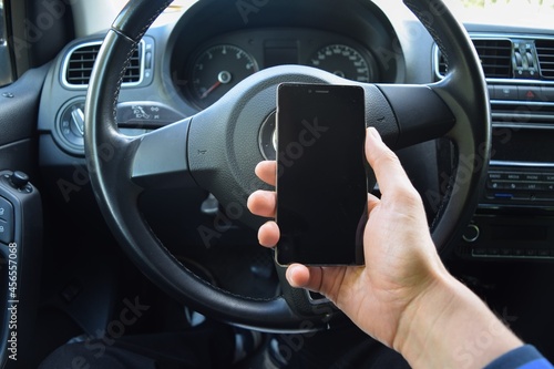  The driver, whose face is not visible, holds a phone in his hand against the background of the steering wheel 