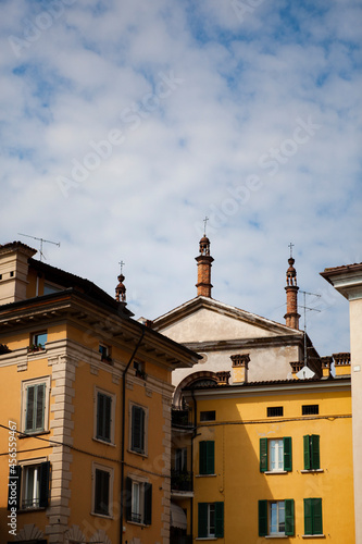 talian traditional architecture. Colorful buildings and a church with towers on the main street in Brescia, Lombardy, Italy. European facade with green shutters, wooden roofs and tiny balconies.